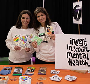 two counselors from the personal counseling center standing in front of sign that says "invest in your mental health"